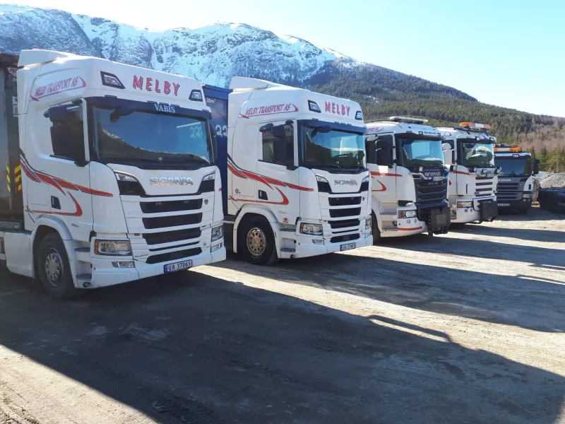 Melby Transport sin bilflåte oppstilt med fjell i bakgrunnen